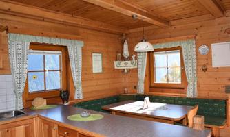 A cozy wooden kitchen with a dining table and green curtains. The windows offer a view of the outdoors and create an inviting atmosphere.