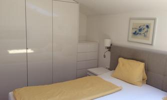 A bright bedroom with a single bed and yellow bedding. There is a wardrobe and a picture on the wall.