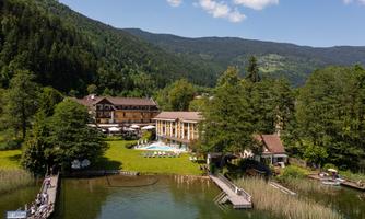 A picturesque hotel by the lake, surrounded by green forests and mountains. The outdoor area features a terrace with access to the water and a swimming pool.