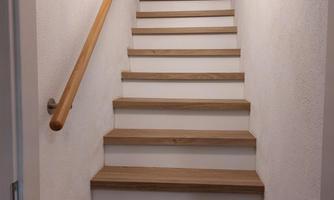 A bright staircase with wooden steps leads upward. The walls are white, and at the top of the staircase, an open door is visible.