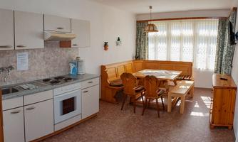 A cozy kitchen with a dining area and plenty of daylight. The light furniture and window curtains create an inviting atmosphere.