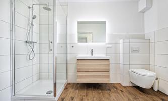 A modern bathroom with a glass shower and a wooden sink. The walls are brightly tiled and the floor is made of wood.