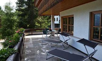 A cozy balcony with loungers and a table amidst green trees. The surroundings are peaceful and inviting.