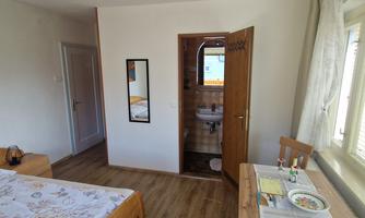 A cozy room with a double bed and a table. In the background, a bathroom with an open door is visible.