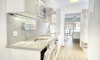 A modern kitchen with bright cabinets and high-quality appliances. In the background, an open living and dining room is visible.