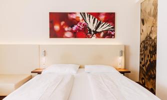 A modern bedroom with a large bed and minimalist decor. On the wall hangs a picture of a butterfly on a red background.