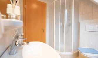 A modern bathroom with a shower and a sink. The walls are tiled in light colors and there is wood paneling on the door.