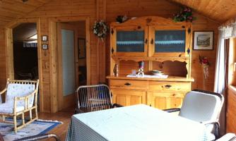 A cozy room with wood paneling and a table in the middle. There are comfortable chairs and a buffet with decorations.