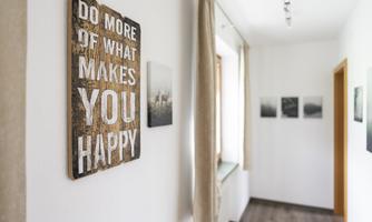 A modern interior design featuring a rustic sign that encourages joy in life. Various pictures hang on the wall, creating a cozy atmosphere.