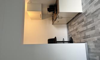 A modern kitchen with bright walls and a wooden floor. The kitchen cabinets are light and well organized.