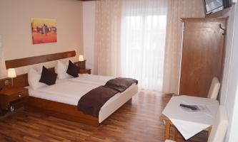 A cozy bedroom with a double bed and wooden floor. The room has plenty of daylight and a small table.