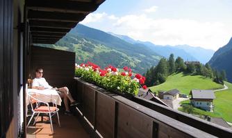 A cozy balcony with colorful flowers and a view of green mountains. A person sits relaxed and enjoys the scenery.