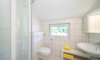 A modern bathroom with a shower, toilet, and sink. Yellow towels are placed on a bench.