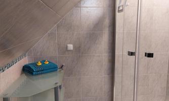 A modern bathroom with a glass shower cabin and gray tiles. Colorful towels and rubber ducks are on a shelf.
