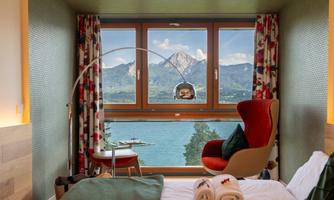 A modern room with a comfortable armchair and a view of a picturesque lake and mountains. Large windows let in plenty of natural light.