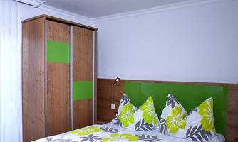 A modern bedroom with a bed that has colorful pillows and a blooming duvet. The walls and furniture are designed in warm earth tones with green accents.