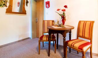 A small entrance area with a round table and two chairs. On the table, there is a flower vase with red flowers.