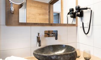 A modern bathroom with an elegant stone sink. In the background, a mirror and a hairdryer are visible.