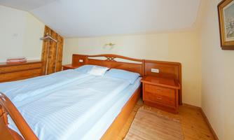 A cozy bedroom with a large double bed and wooden furniture. The walls are painted in a light color and the floor is made of wood.