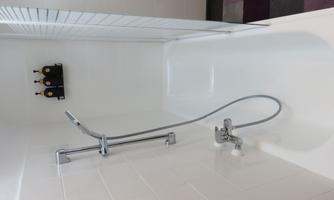 A modern bathroom with a white bathtub and a shower. On the wall, three bottles are placed on a shelf.