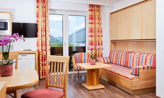 A bright living room with a cozy couch and a dining table. Large windows offer a view of the mountains and the room is cheerfully decorated.