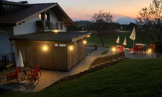 A cozy building at dusk with illuminated tables and chairs in the outdoor area. The sky displays soft colors of the sunset.