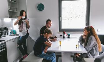 A family is sitting together at the table in a modern kitchen. The adults are chatting while the children listen attentively.