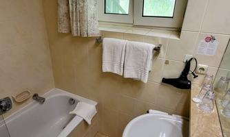 The bathroom is small and tiled in beige. It contains a bathtub, a sink, and two towels on the wall.