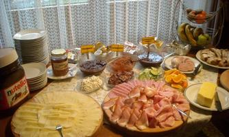 A rich breakfast buffet featuring various cheeses, cold cuts, and fresh fruits. There is also Nutella and different spreads.