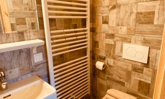 A modern bathroom with a wood look and large tiles. It contains a sink, a toilet, and a towel warmer.
