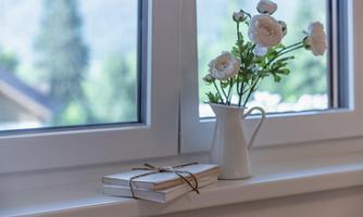 On the windowsill lie several books that are tied together with a band. Next to them stands a small vase with white flowers.