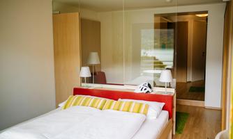 A modern bedroom with a bed and colorful pillows. In the background, there is a bright hallway and mirrors that expand the space.