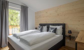 A modern bedroom with a large bed and wooden walls. The room has windows with curtains and a small table.