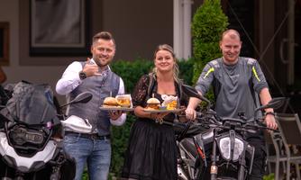 Three people are standing next to motorcycles and holding plates with food. They are smiling and showing satisfaction.