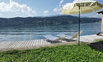 A tranquil landscape by the sea with deck chairs and a sun umbrella. In the background, there are gentle hills and a clear sky.