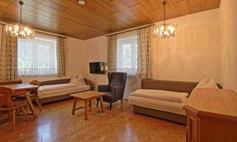 A bright living room with cozy seating and a table. There are large windows that let in plenty of light, and a warm wooden ceiling.