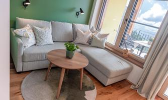A cozy living area with a bright sofa, colorful cushions, and a round coffee table. Large windows let in plenty of natural light.