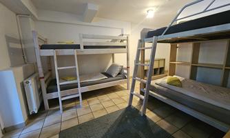 A simple room with two bunk beds and a carpet. The walls are light, and there is a window for natural light.