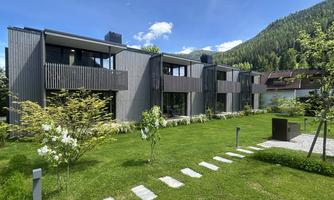 Modern buildings with wooden cladding in a green environment. The garden is well-maintained and offers a beautiful view of the surrounding mountains.