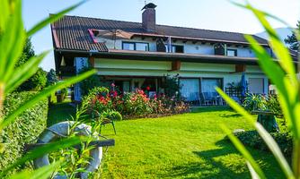 A beautiful house with a well-maintained garden and colorful flowers. The sky is blue and the sun is shining.
