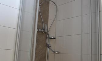 A modern shower with glass doors and a flexible hand-held showerhead. The walls are brightly tiled and the fixtures have a simple and functional appearance.