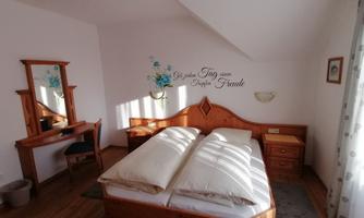 A cozy bedroom with a double bed and wooden furniture. There is a mirror and a decorative wall design.