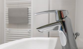 A modern sink with a shiny faucet. In the background, towels and a mirror are visible.