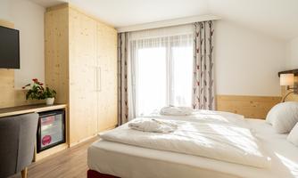 A bright room with two single beds and a large window. A television and a small refrigerator are also provided.