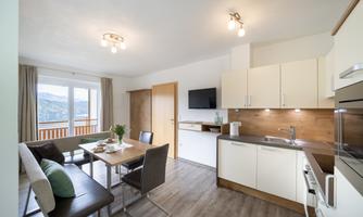 A modern kitchen with a dining area and large windows. The room is bright and offers a view of the mountains.