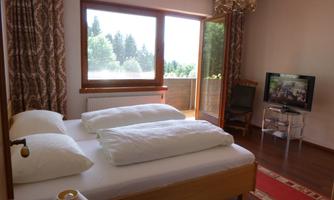 A bright bedroom with a double bed and large windows. A TV and an armchair are in the room.