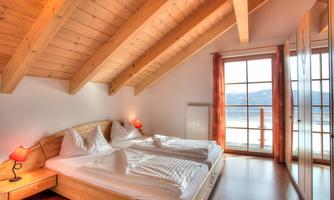 A cozy bedroom with a double bed and wooden ceilings. Large windows offer a beautiful view of the landscape.