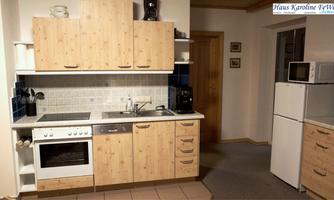 A modern kitchen with wooden cabinets and a bright design. It is equipped with a stove, a sink, and a refrigerator.