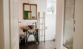 A modern bathroom with clean lines and neutral colors. There is a wash area with a sink, a mirror, and a decorative ladder.