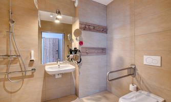 A modern bathroom with a walk-in shower and light tiled floor. The amenities include a sink, a toilet area, and grab bars for added safety.